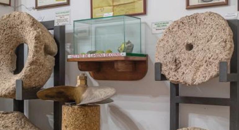 Muestra una vitrina con objetos pequeños y a ambos lados dos piedras de molino del Museo de de Raíces Conileñas 