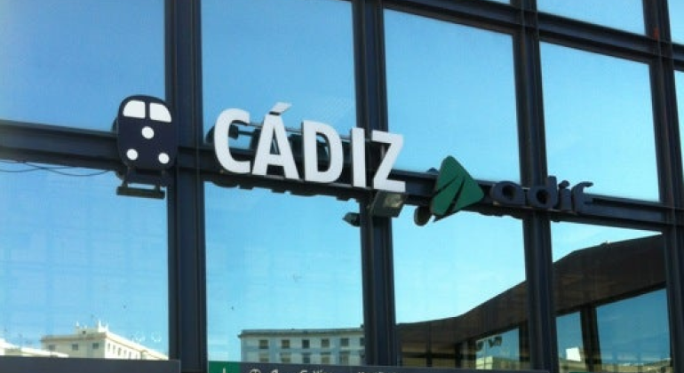 Frontal estación de trenes de Cádiz con unas cristaleras que contiene unas letras blancas que forman la palabra Cádiz y el logo de Adif