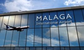 Frontal del Edificio del Aeropuerto de Málaga con unas cristaleras que contiene unas letras blancas que forman la palabra Málaga International Airpot y se refleja un avión