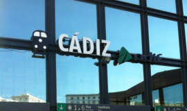 Frontal estación de trenes de Cádiz con unas cristaleras que contiene unas letras blancas que forman la palabra Cádiz y el logo de Adif