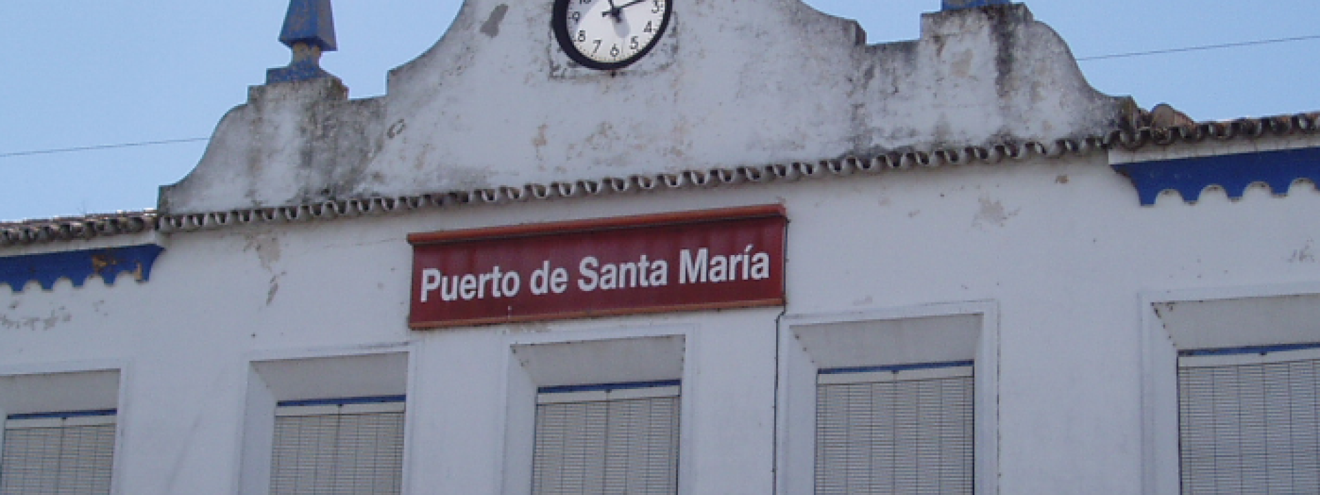 Fachada de la estación del Puerto de Santa María con un reloj en la parte superior y ventanas blancas
