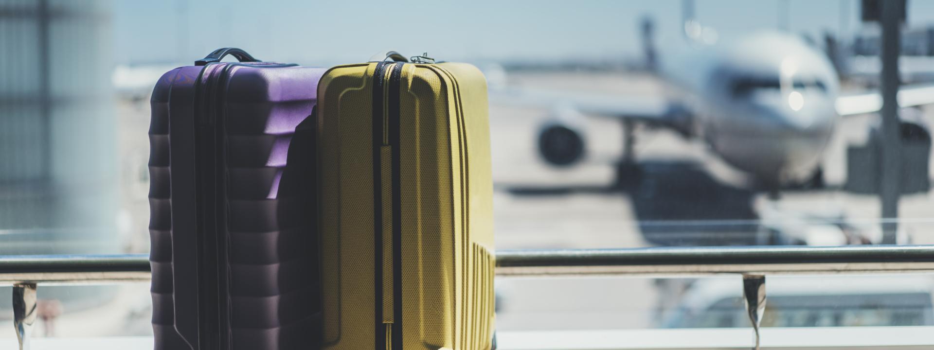2 maletas morada y amarilla delante de una cristalera donde se visualizan aviones en la pista