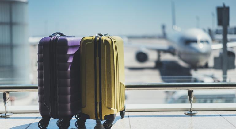 2 maletas morada y amarilla delante de una cristalera donde se visualizan aviones en la pista